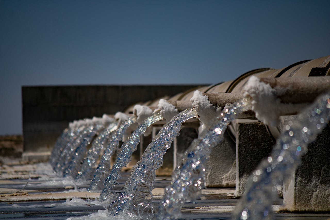 Close-up view of water flowing from industrial pipes against a clear blue sky.