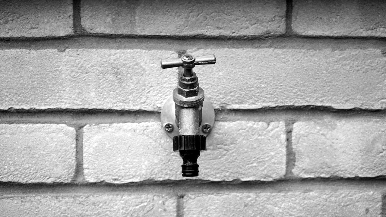 Black and white photo of a metal water faucet on a brick wall, emphasizing texture.